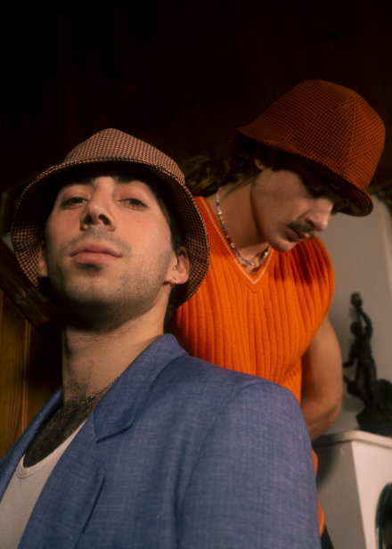 Julio & paul are wearing a Le Panache Paris© bucket hats made in France with Go couture_7101 & 63080, fabric from Gabriel© brand, 100% Trevira cs, brown houndstooth pattern on a pink & orange background.