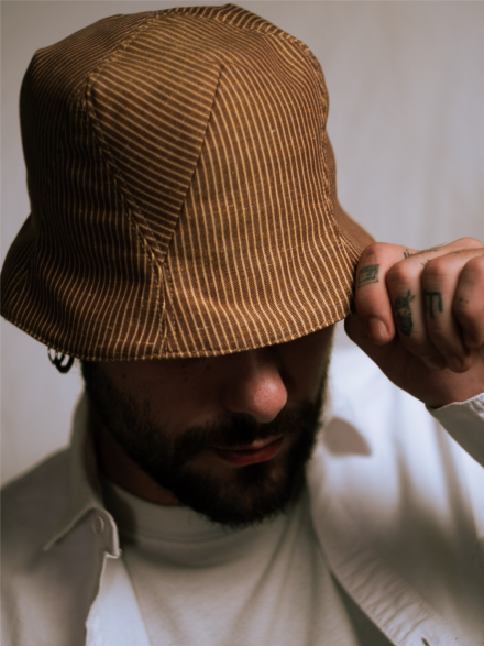 Tristan is wearing a Le Panache Paris© bucket hat made in France with tobacco and ivory stripeweave100% cotton.