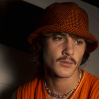 Paul is wearing a Le Panache Paris© bucket hat made in France with Go Couture_63080, Gabriel© brand fabric, 100% Trevira cs, brown houndstooth pattern on a orange background.